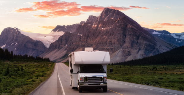 White RV Driving on a scenic road in the Canadian Rockies during a vibrant sunny summer sunrise with the mountains in the background. 